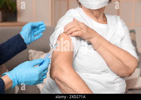 Junge Krankenschwester geimpft ältere Frau zu Hause, Nahaufnahme Stockfoto