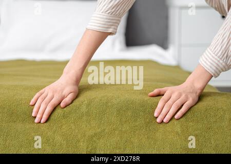 Junge Frau, die zu Hause grüne Decke auf das Bett legt, Nahaufnahme Stockfoto