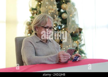 Glückliche Frau kauft Weihnachtsgeschenke mit Handy und Kreditkarte Stockfoto