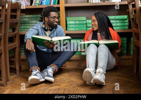 Zwei junge Leute sitzen auf dem Boden in der Bibliothek und lesen ein Buch Stockfoto