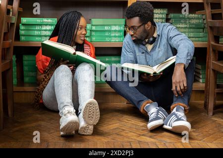 Zwei junge Leute sitzen auf dem Boden in der Bibliothek und lesen ein Buch Stockfoto