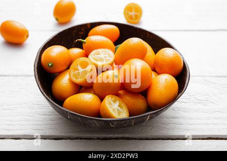 Kumquats oder Kumquats ( Citrus japonica) in einer Kokosnussschale und auf weißem Holzbrett Hintergrund. Studio-Aufnahme, Studio-Licht. Stockfoto