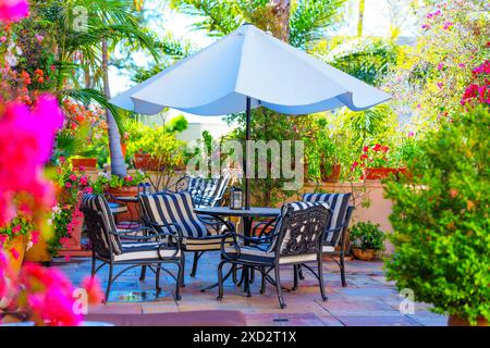 Einladende Außenterrasse mit bequemen Sitzgelegenheiten, weißem Sonnenschirm und blühenden Blumen. Stockfoto