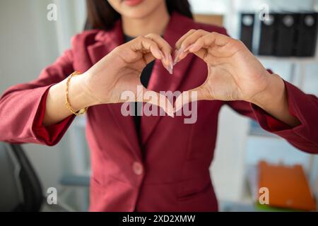 Eine junge Frau hebt ihre Hände, um ein Herzsymbol zu machen, das Liebe und Freundschaft bedeutet. Das Konzept von ​​using Händen zur Herstellung eines Herzsymbols stellt den Mittelwert dar Stockfoto