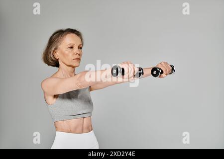 Eine ältere Dame macht Hantelübungen auf grauem Hintergrund. Stockfoto