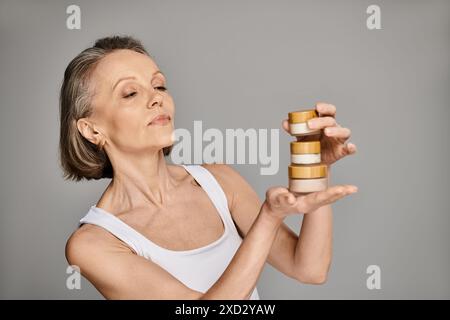 Eine reife Frau in bequemer Kleidung hält anmutig eine Flasche Creme. Stockfoto