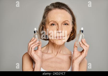 Eine reife, attraktive Frau hält elegant zwei Flaschen Hautpflegeprodukte. Stockfoto