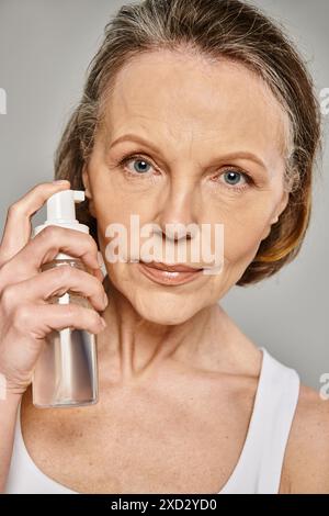 Eine reife, attraktive Frau in bequemer Kleidung hält eine Flasche Hautpflegemittel. Stockfoto