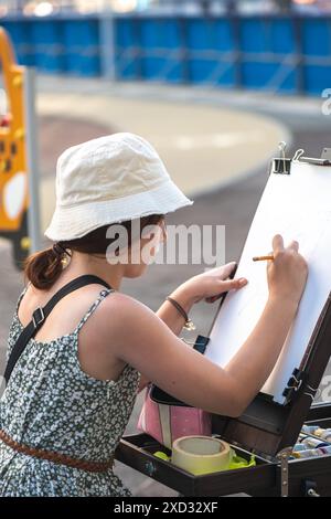 Niedliches Teenager-Mädchen, das draußen an der Staffelei zeichnet, im Innenhof des Hauses in der Stadt, Kunst, Plein Air, DIY Stockfoto