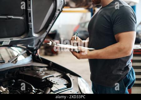 Klemmbrett, Hände und Mechaniker in Garage mit Autoservice, Wartung oder Kfz-Versicherung. Checkliste, Motor und Mann in der Werkstatt für Inspektion, Motor Stockfoto