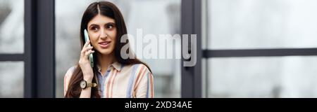 Eine Frau plaudert auf einem Handy vor einem Fenster. Stockfoto