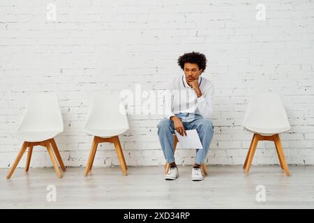 Mann saß vor weißem Stuhl an einer Ziegelwand. Stockfoto