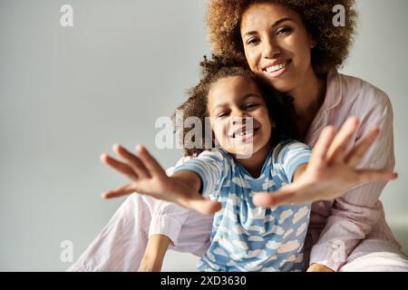 Eine glückliche afroamerikanische Mutter und Tochter im Pyjama posiert zusammen für die Kamera vor grauem Hintergrund. Stockfoto