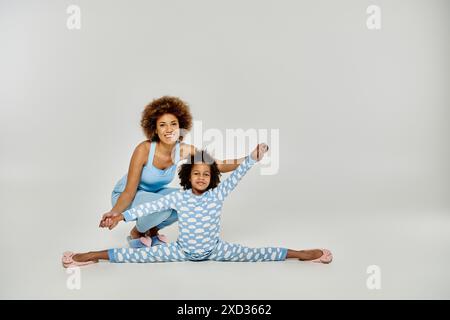 Eine glückliche afroamerikanische Mutter und Tochter im Pyjama, die zusammen Yoga auf weißem Hintergrund üben. Stockfoto