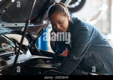 Auto, Mechaniker und Telefonanruf mit Frau in der Werkstatt für Wartung, Reparatur oder Wartung des Motors. Auto, Experte und Inspektion mit asiatischem Fahrzeug Stockfoto