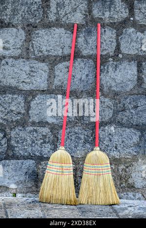 Zwei Besen mit roten Griffen, die an eine Steinmauer gebeugt sind Stockfoto
