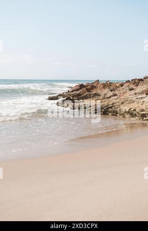 Ruhige Strandszene mit Wellen, die sanft gegen die felsige Küste unter klarem Himmel schlagen Stockfoto