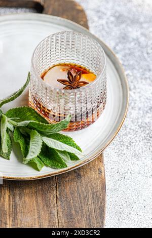 Ein raffiniertes Glas Kirschcocktail mit Eis, Minzblättern und Anisstern, elegant auf einem Holztablett präsentiert. Stockfoto