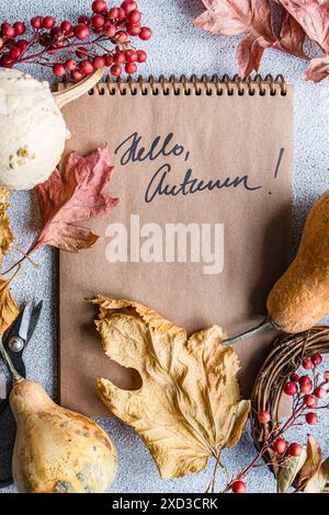 Handwerklich gestaltetes, herbstliches Flaglay mit natürlichen Elementen wie getrockneten Blättern und Kürbissen, einem Notizbuch mit HELLO, HERBSTBOTSCHAFT und saisonaler Dekoration Stockfoto