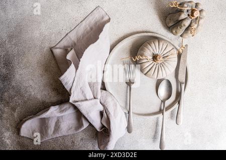 Eine geschmackvolle herbstliche flache Liege mit einem Tisch in neutralen Farben mit dekorativem Kürbis, grauen Tellern und Leinenserviette, ideal für saisonale Designs Stockfoto