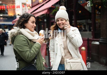 Mutter und Tochter genießen Eis und telefonieren in der Londoner Straße. Stockfoto