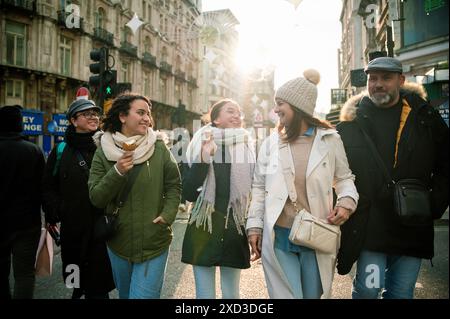 Eine fröhliche Familie spaziert durch die sonnigen Straßen Londons und teilt an einem Wintertag Lacher und Leckereien. Stockfoto