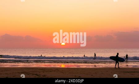 Ruhige Strandszene bei Sonnenuntergang mit Surfern und sanften Wellen, die das ruhige Wesen der sommerlichen Küstenlandschaften einfangen Stockfoto