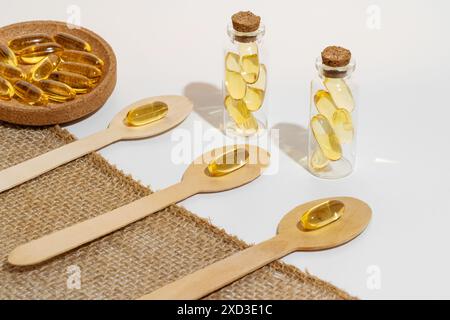 Dieses Bild zeigt Omega-3-Kapseln, die in Glasflaschen und Holzlöffeln angeordnet sind, vor einem Hintergrund mit Sackleinen-Textur Eine ganzheitliche Präsentation emp Stockfoto