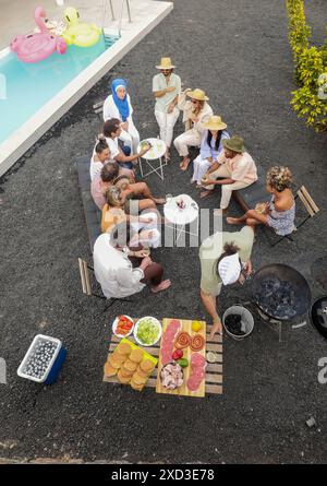 Blick von oben auf eine vielfältige Gruppe von Freunden, genießen ein BBQ am Pool, mit verschiedenen ethnischen Gruppen, einschließlich Kaukasier, Hispanic, Afrikaner Stockfoto