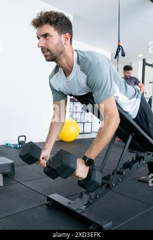 Ein fokussierter Mann nimmt ein Krafttraining mit Kurzhanteln in einem gut ausgestatteten Fitnessstudio an, was Hingabe und Fitness veranschaulicht Stockfoto