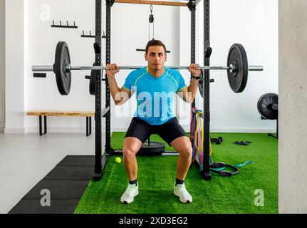 Ein fokussierter Mann führt eine Langhantelhocke in einem gut ausgestatteten, modernen Fitnessraum aus und zeigt Kraft und Hingabe Stockfoto