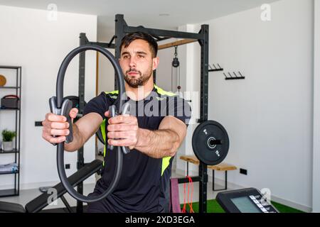Ein athletischer Mann konzentriert sich auf das Training mit Fitnessringen in einem gut ausgestatteten Fitnessstudio zu Hause und unterstreicht das Engagement für Fitness Stockfoto