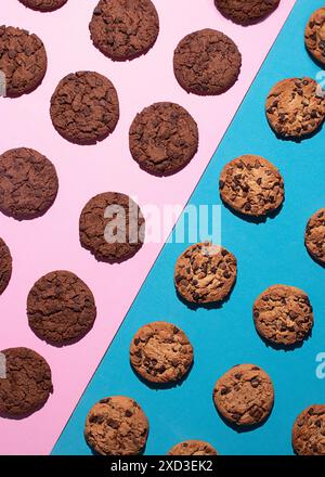Draufsicht auf verschiedene Schokoladenchips und doppelte Schokoladenkekse, die symmetrisch auf einer kontrastierenden rosa und blauen Oberfläche platziert sind. Das Bild hebt den hervor Stockfoto