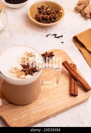 Von oben Ein dampfender Becher Chai Latte, belegt mit Sternanis und bestreut mit Zimt auf einem Holzbrett, in einem rustikalen Stil Stockfoto