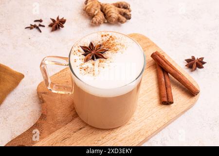 Von oben: Chai Latte mit aufgeschäumter Milch, Sternanis und Zimtstangen auf einem Holzbrett mit frischen Zutaten Stockfoto