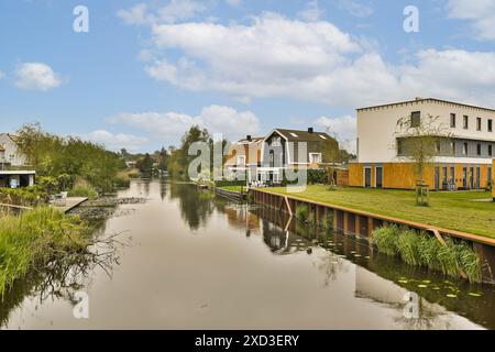Einige Häuser auf der Seite eines Gewässers mit Bäumen und Büschen im vorderen Teil des Flusses Stockfoto