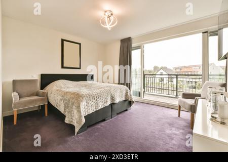Ein Schlafzimmer mit violettem Teppich und einem Bett vor einer Glasschiebetür, die zu einem Balkon führt Stockfoto