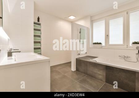 Ein modernes Badezimmer mit grauem Fliesenboden und weißen Wänden sowie einer freistehenden Badewanne in der Ecke Stockfoto