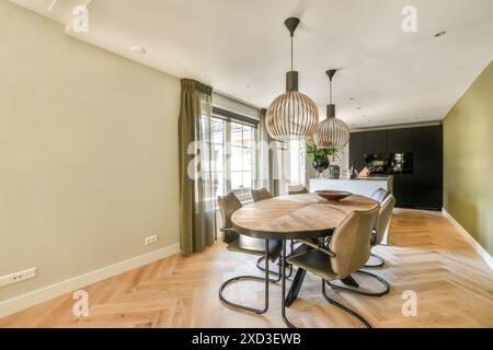 Eleganter Speisesaal mit ovalem Holztisch, Ledersesseln und auffälligen Pendelleuchten. Durch große Fenster strömt natürliches Licht ein, was die Aufmerksamkeit verstärkt Stockfoto