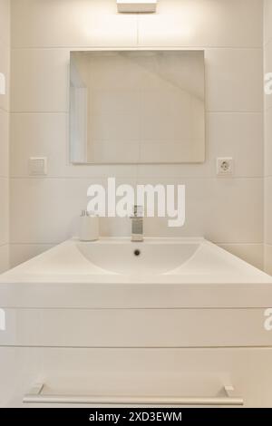 Ein Badezimmer mit Waschbecken und Spiegel an der Wand daneben ist ein Bild der Reflexion eines Mannes im Spiegel Stockfoto