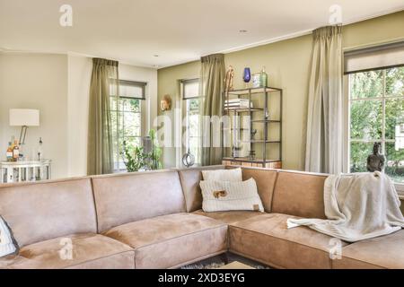 Ein gut beleuchtetes, gemütliches Wohnzimmer mit modernem Wildledersofa, stilvollem Regal, schicken Vorhängen und dekorativen Accessoires. Stockfoto