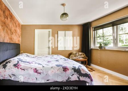 Ein gut beleuchtetes, modernes Schlafzimmer mit elegantem Bettüberwurf mit Blumenmuster, strukturierter Tapete und minimalistischem Kleiderschrank. Stockfoto