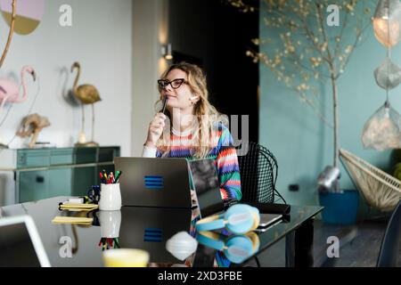 Eine junge Frau konzentriert sich auf ihre Arbeit von zu Hause aus mit einem Laptop, umgeben von Natur-inspirierter Einrichtung Stockfoto