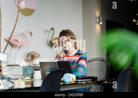 Eine nachdenkliche Frau arbeitet von zu Hause aus, umgeben von stilvoller Einrichtung und naturinspirierten Elementen, die ein Beispiel für modernes, intelligentes Arbeiten darstellen Stockfoto