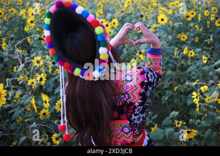 Eine junge Frau im Tribal-Outfit hebt ihre Hände, um ein herzförmiges Zeichen zu machen, das Liebe und Freundschaft vor dem Hintergrund eines wunderschönen Morgenflusses symbolisiert Stockfoto