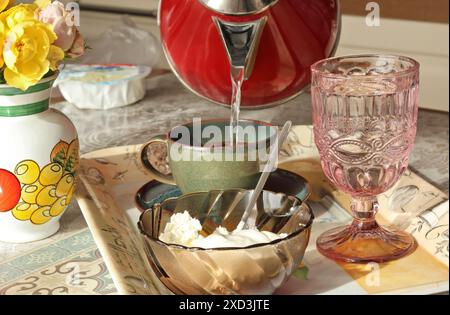 Anonym gießen kochendes Wasser in eine Tasse mit gemahlenem Kaffee. Frühstück auf einem Tablett. Innenraum der Küche. Ernährung und Gesundheit. Stockfoto