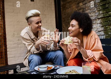Zwei schöne Frauen verschiedener Ethnien sitzen zusammen an einem Tisch und teilen sich eine Mahlzeit in einem gemütlichen Café. Stockfoto