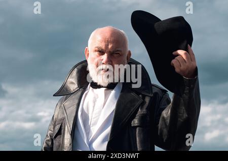 Foto von Seriuos brutal aussehenden Opa. Älterer Mann mittleren Alters mit grauem Bart und Ledermantel mit Fliege Stockfoto