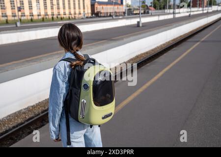Frau, die mit einer Katze reist, die im Rucksack für Haustiere sitzt, auf dem Bahnsteig des Bahnhofs steht. Stockfoto