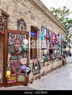 Baku, Aserbaidschan - 4. Mai 2024: Eine offene Tür zeigt ein Geschäft im historischen Stadtteil Icherisheher in Baku, in dem farbenfrohe Teppiche, Taschen und andere traditionelle Waren zum Verkauf angeboten werden Stockfoto